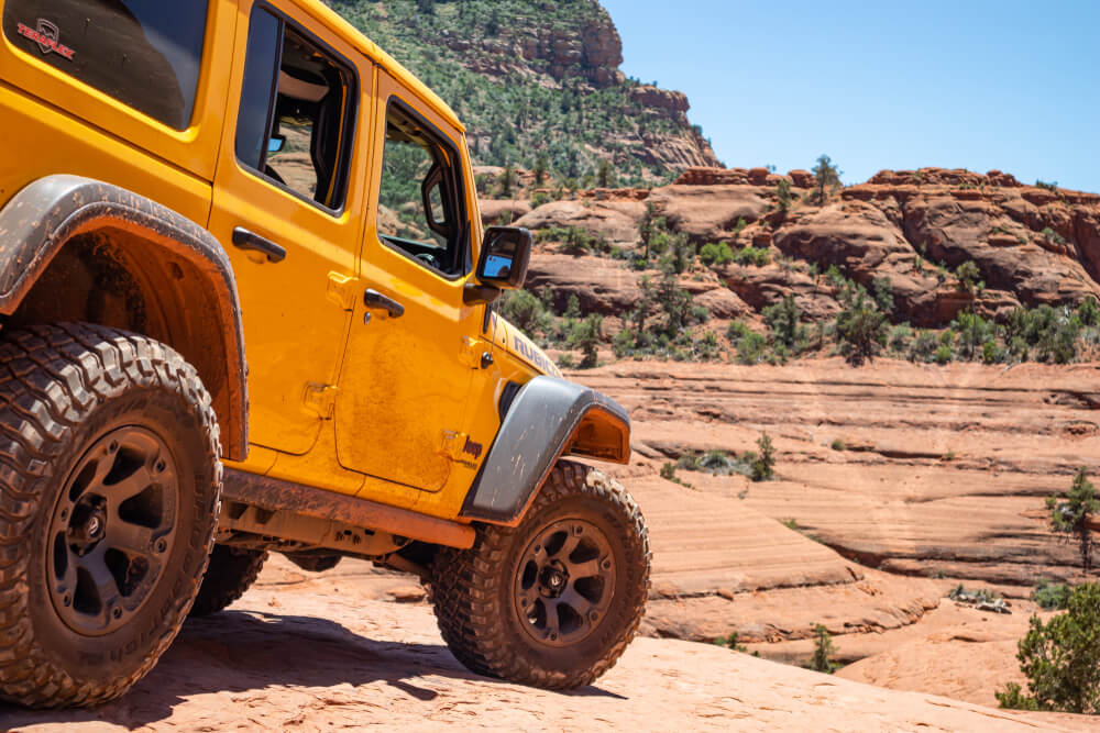 4 wheel drive jeep car on red orange rocks, desert landscape, clear blue sky, sunny spring day