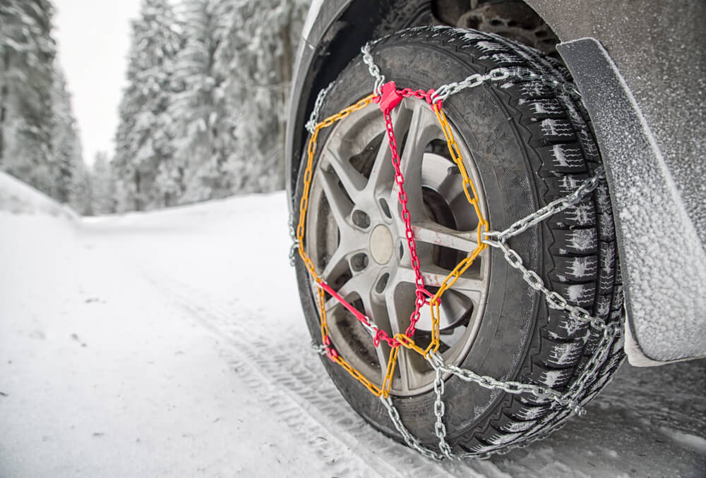 Snow chains on tire. Detail of wheel in winter forest